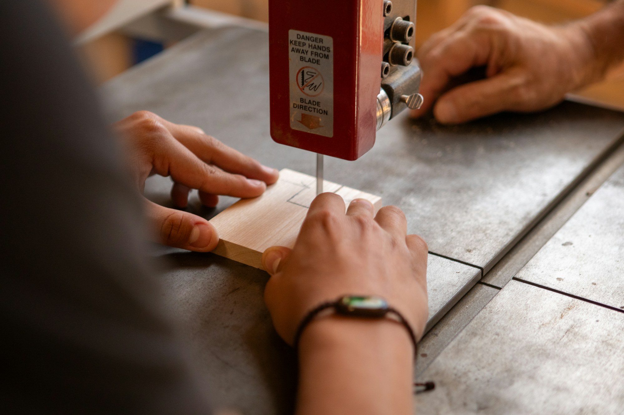 Skilled hands guiding timber through a workshop bandsaw